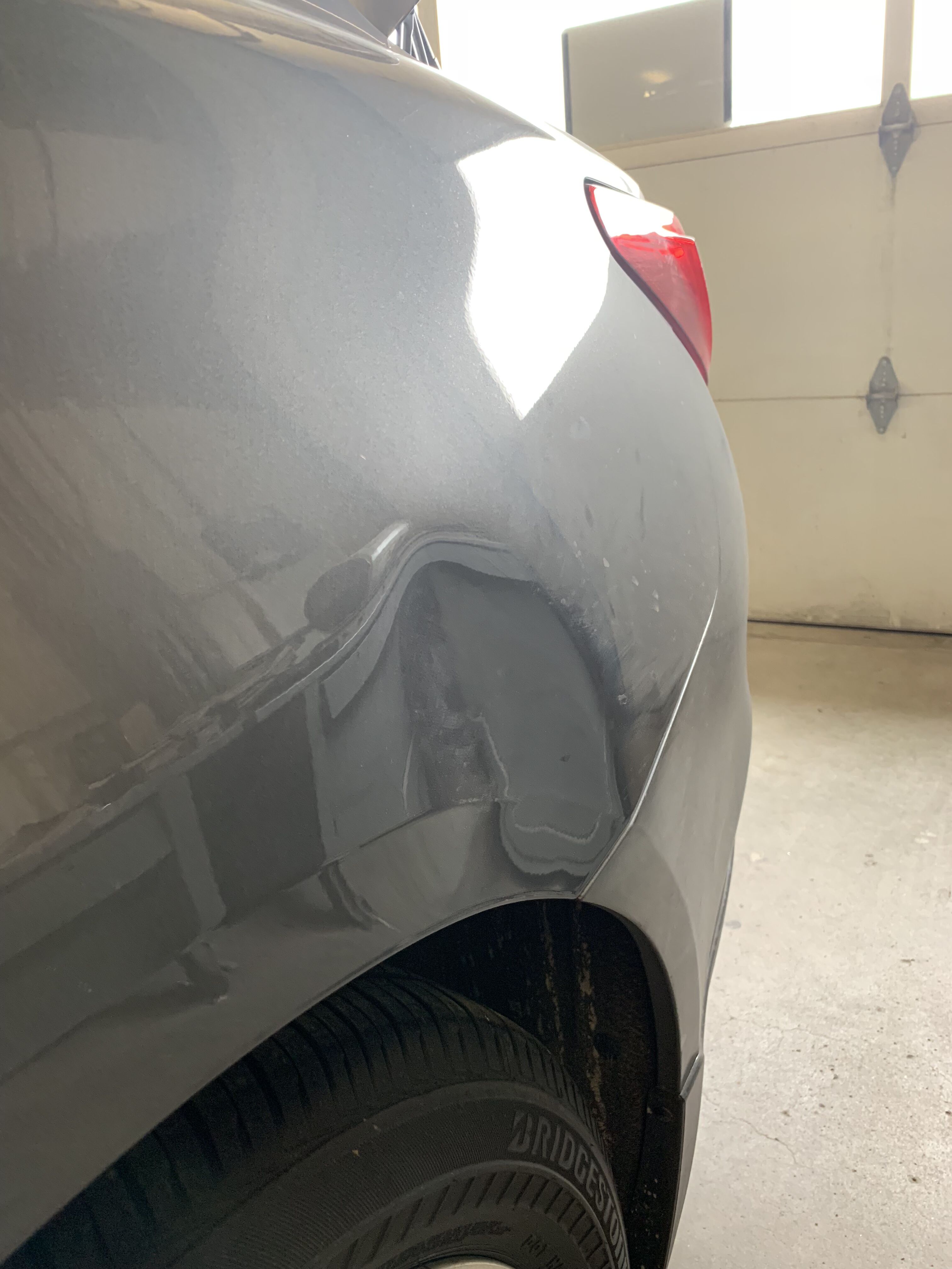 a gray car with a large dent on the rear fender